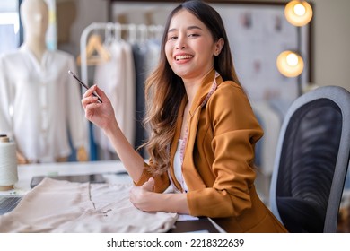 Young professional clothes fashion designer sitting near sewing machine use laptop computer   tablet pc to reference design smiling portrait to camera