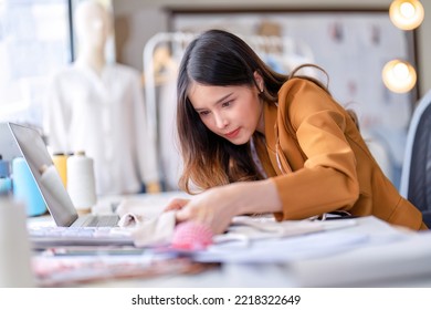 Young professional clothes fashion designer sitting near sewing machine use laptop computer   tablet pc to reference   concentrate her work pattern