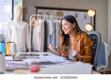 Young professional clothes fashion designer sitting near sewing machine use laptop computer   tablet pc to reference   she got the good news as world winner clothes designer