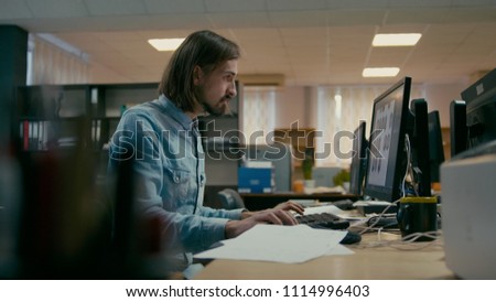 Young Professional Designer is Working at the Computer in the Office Alone in the Evening