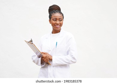 Young professional female black doctor with braided updo hair holds clipboard and wears a lab coat while smiling and looking to the right                               