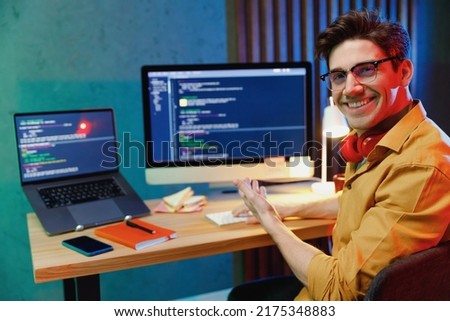 Young professional happy site reliability engineer engineer IT specialist programmer man in shirt work at home writing code point hand on laptop pc computer show project. Program development concept