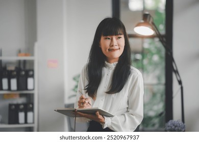 Young professional is holding a notebook and pen, deep in thought while working in a modern office environment - Powered by Shutterstock