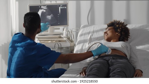 Young professional male african doctor, looking at screen performing ultrasound scan of abdomen of pregnant woman in clinic. Pregnancy and healthcare concept - Powered by Shutterstock