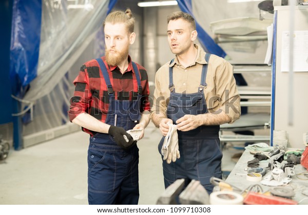 Young professional male automotive technicians\
looking at something attentively while getting ready for work in\
repair shop
