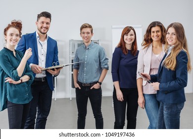 A Young, Professional Male College Teacher And Small Group Of Students Smile At The Camera In A Modern Classroom.