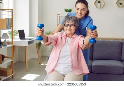 Young professional nurse, caregiver or physiotherapist helping a happy old pensioner woman do rehabilitation fitness exercises with light weight dumbbells. Concept of physiotherapy for seniors - Powered by Shutterstock