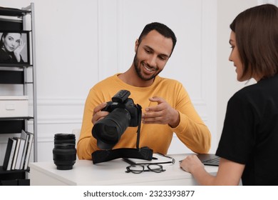 Young professional photographer showing camera to woman in modern photo studio