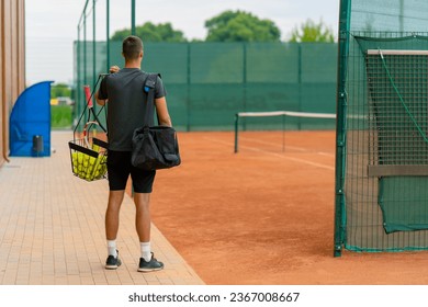 young professional player coach standing on outdoor tennis court before starting game training with racket and basket tennis balls - Powered by Shutterstock