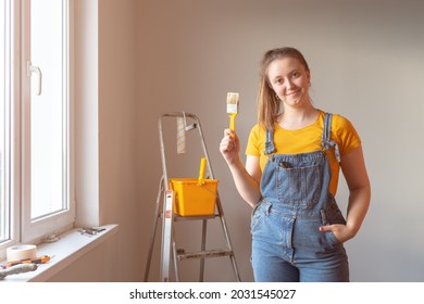 Young Professional repairwoman with a brush for painting on background ladder and gray cement wall. Independent single female makes repairs in her apartment  - Powered by Shutterstock