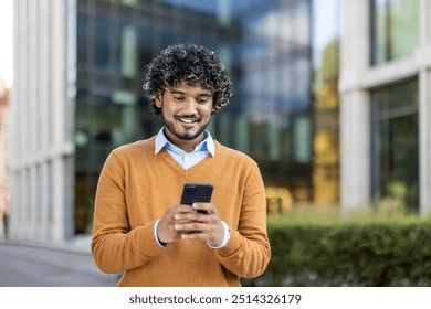 Young professional smiling while using smartphone in urban setting. Dressed in casual attire, enjoying communication and connectivity during outdoor break near office buildings. - Powered by Shutterstock