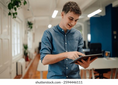 Young professional is smiling while using a digital tablet in a bright, modern office, suggesting a productive and engaging work environment