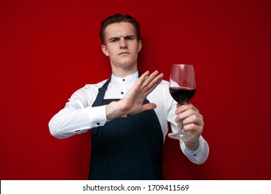 Young Professional Sommelier With A Glass Of Red Bad Wine Refuses To Drink On A Red Background, The Guy The Waiter Does Not Recommend Drinking Alcohol