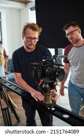 Young Professional Videographer Moving Video Camera Along Slider While Adjusting Its Options For Shooting Of Advertisement In Studio