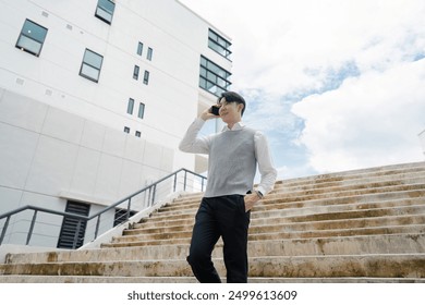 Young Professional Walking Downstairs While Talking on Mobile Phone Outside Modern Office Building - Powered by Shutterstock