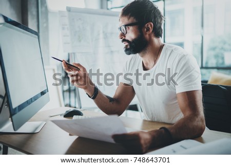 Young professional web designer wearing eye glasses working at modern loft studio-office with desktop computer.Blurred background. Horizontal