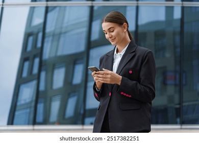 A young professional woman in a business suit smiles while using her smartphone in an urban setting.

 - Powered by Shutterstock