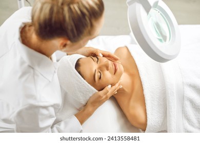 Young professional woman cosmetologist examining skin condition to a smiling girl client in beauty clinic. Beautician making facial massage or skin care procedure for treatment in spa salon. - Powered by Shutterstock