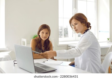 Young professional woman doctor with serious consulting a teen girl on checkup appointment showing something in laptop screen. Pediatrician consultation visit in clinic. Healthcare, medicine concept. - Powered by Shutterstock