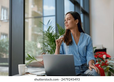 Young professional woman is focused on her laptop work at a bright modern office desk by the window - Powered by Shutterstock