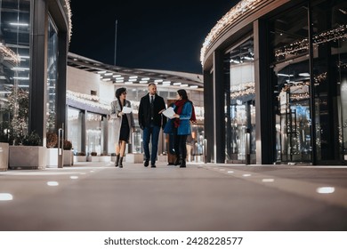 Young professionals in business attire walk and converse outside an office building adorned with festive lights, creating a blend of corporate and holiday vibes.. - Powered by Shutterstock