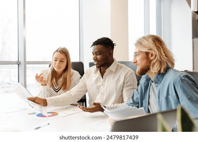 Young professionals collaborating in a bright office, analyzing financial charts, brainstorming ideas for startup success. Smiling and communicating effectively. Teamwork concept - Powered by Shutterstock