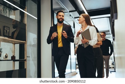 Young professionals having a discussion in a modern office. Two happy young businesspeople smiling while walking together in a hallway. Cheerful colleagues collaborating on a new project. - Powered by Shutterstock