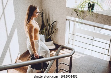 Young professionals, traineeship, practical experience. Young business woman walking up the stair in office. Young beautiful woman with handbag and documents walking indoors