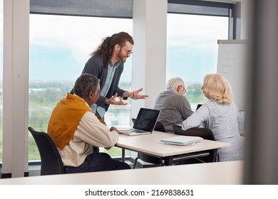 A Young Professor Is Explaining To Small Group Of Senior Students How To Use Laptops And Technology In A Classroom.