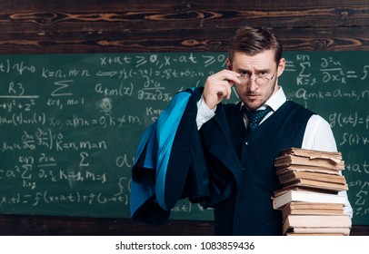 Young professor holding pile of books looking over his glasses. Aristocrat scholar in elite college.