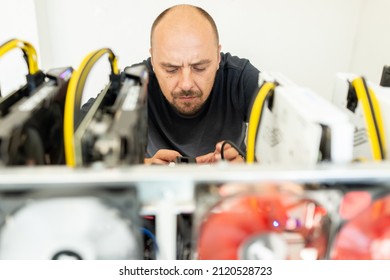 Young programmer adjusting cryptocurrency mining rig to optimal operational settings. High quality photo
