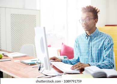 Young programmer sitting by desk in front of computer monitor and searching for online data