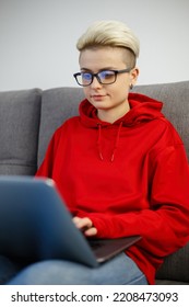 Young Programmer Woman Coding On Laptop While Sitting On Couch At Home. Download Stock Photo Of Whire Nerd Girl Working On Notebook Pc. Focused Female Person Typing Text On Computer