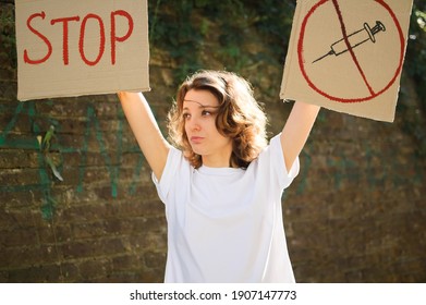 Young protesting woman in white shirt and jeans holds protest sign broadsheet placard with slogan 'Stop' and syringe sing as a symbol of vaccine for public demonstration on wall background