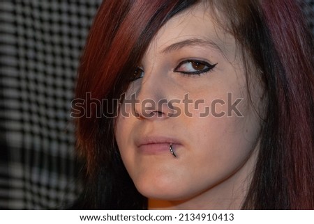 Young punk emo Girl with piercing, with red and black hair, looking at camera with serious facial expression, close-up