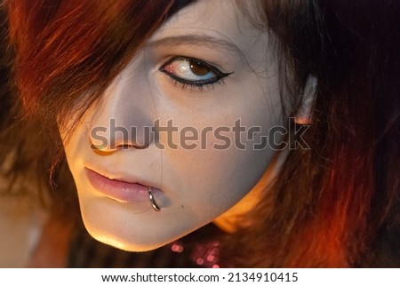 Young punk emo Girl with piercing, with red and black hair, looking at camera with serious facial expression, close-up