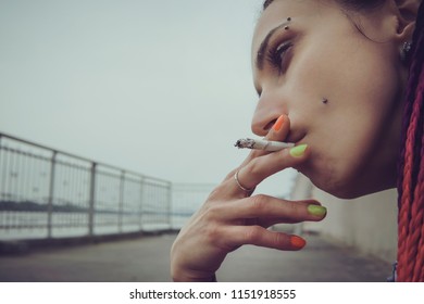 Young punk girl smoking cigarette. Hipster with pink dyed hair. Woman with piercing and unusual hairstyle. sadness, loneliness sadness on the face of a young informal model. subculture - Powered by Shutterstock