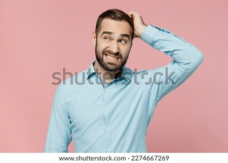 Young puzzled caucasian man 20s wear classic blue shirt look aside on workspace area mock up scratch hold head isolated on plain pastel light pink background studio portrait. People lifestyle concept
