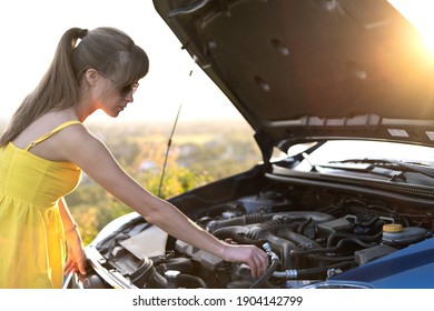 Young Puzzled Woman Driver Standing Near Her Car With Popped Up Hood Looking At Broken Engine.