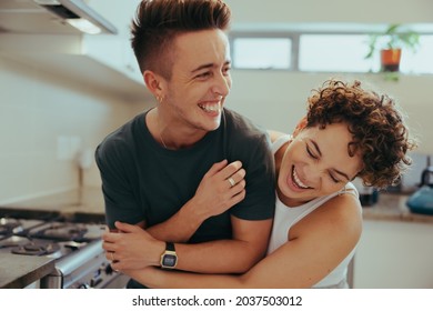 Young queer couple laughing together indoors. Happy young queer couple having fun together while standing in their kitchen. Romantic young LGBTQ+ couple bonding fondly at home. - Powered by Shutterstock