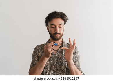 Young queer latin gay man painting his nails on a white background.