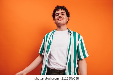 Young queer man looking at the camera with a cheerful face in a studio. Happy young generation z hipster smiling while standing alone against an orange background.