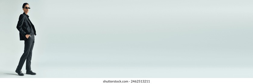 A young queer person stands confidently in a black suit against a stark white background. - Powered by Shutterstock