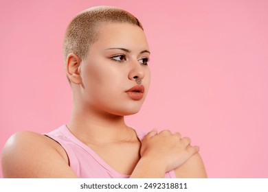 Young queer woman with a shaved head and nose piercing is posing in a studio, embracing body positivity and self expression - Powered by Shutterstock