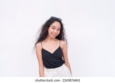A young and radiant Filipino woman with long curly hair in her early 20s. Wearing a black spaghetti strap blouse. Isolated on a white background. - Shutterstock ID 2243876841