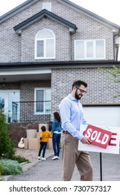 Young Realtor With Sold Signboard In Front Of People Moving Into New House