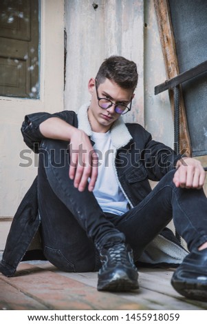 a young rebel in a jacket and jeans on the background of an old crumbling building with glasses and brutal hair