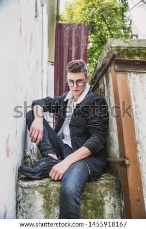 a young rebel in a jacket and jeans on the background of an old crumbling building with glasses and brutal hair