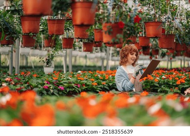 Young red haired florist is enjoying her checkup in hothouse full of flower pots with various blooming flowers. Florist holding checklist and writing down info about her colorful flower garden. - Powered by Shutterstock