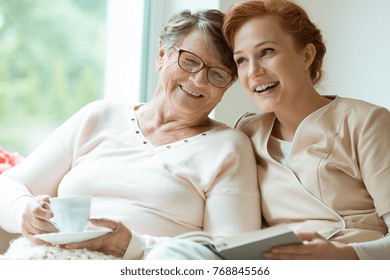 Young red haired nurse spending time with happy elder patient in nursing home